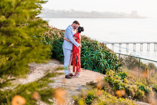 bride in qipao kissing groom with Scripps Pier La Jolla in background