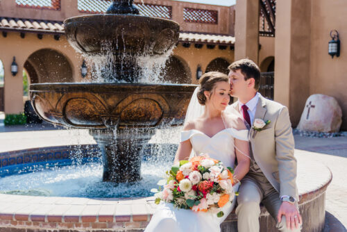 groom kissing bride while sitting in front of water fountain at st gabriels catholic church poway