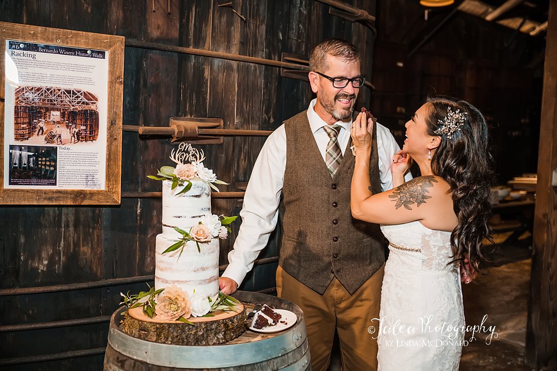 bride feeding groom wedding cake barrel room at bernardo winery san diego