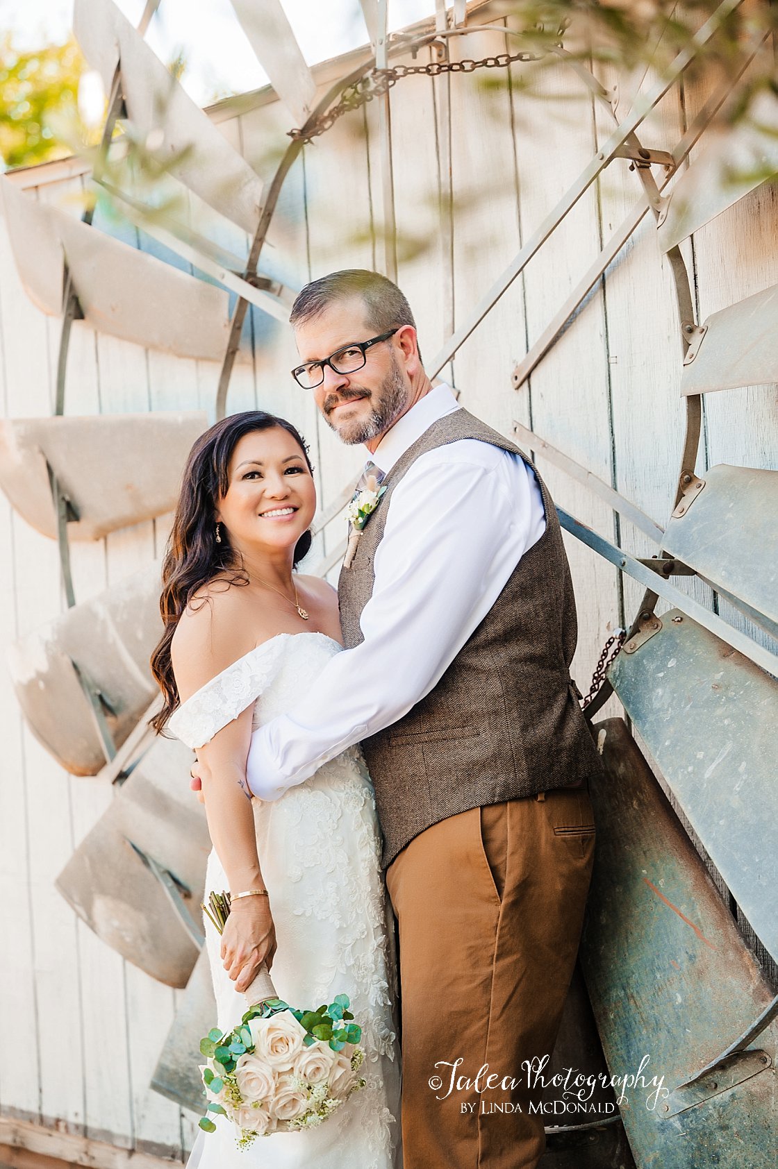 bride and groom embracing and smiling towards camera in front of windmill at san diego wedding venue