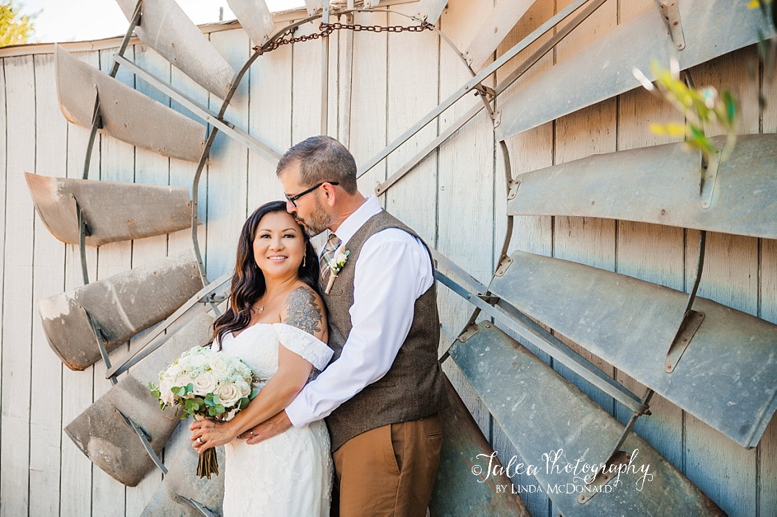 groom kissing bride on temple in front of windmill at rustic wedding venue san diego