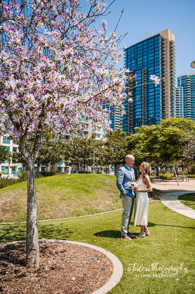 A couple stands under a jacaranda tree at the San Diego Waterfront Park