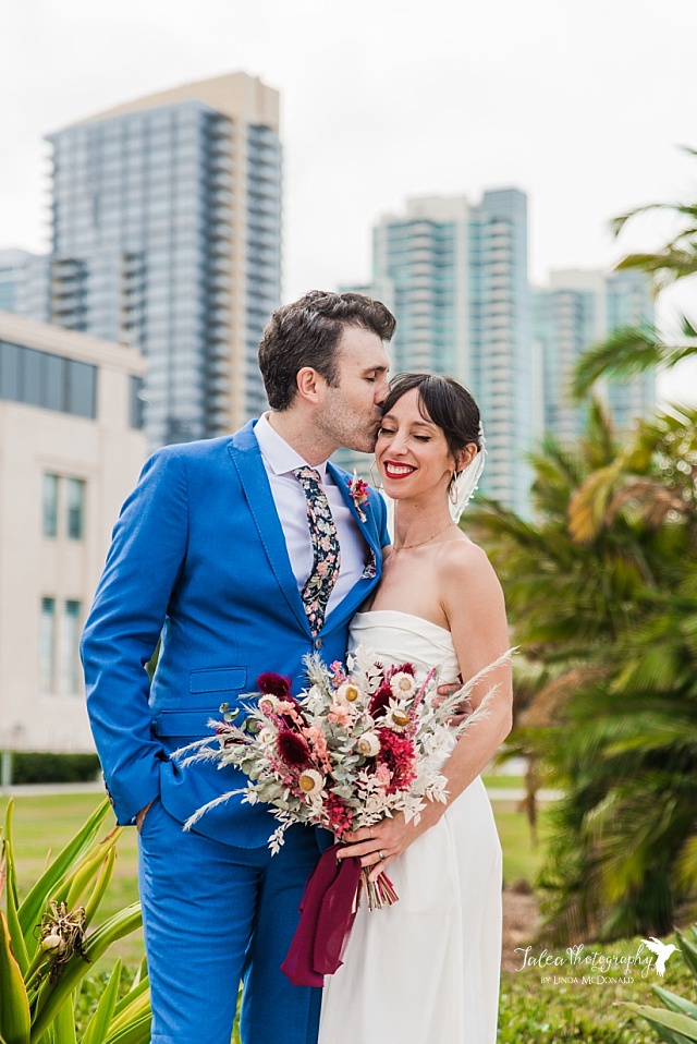 A couple in casual wedding attire pose at the County Administration Center with downtown San Diego in the distance