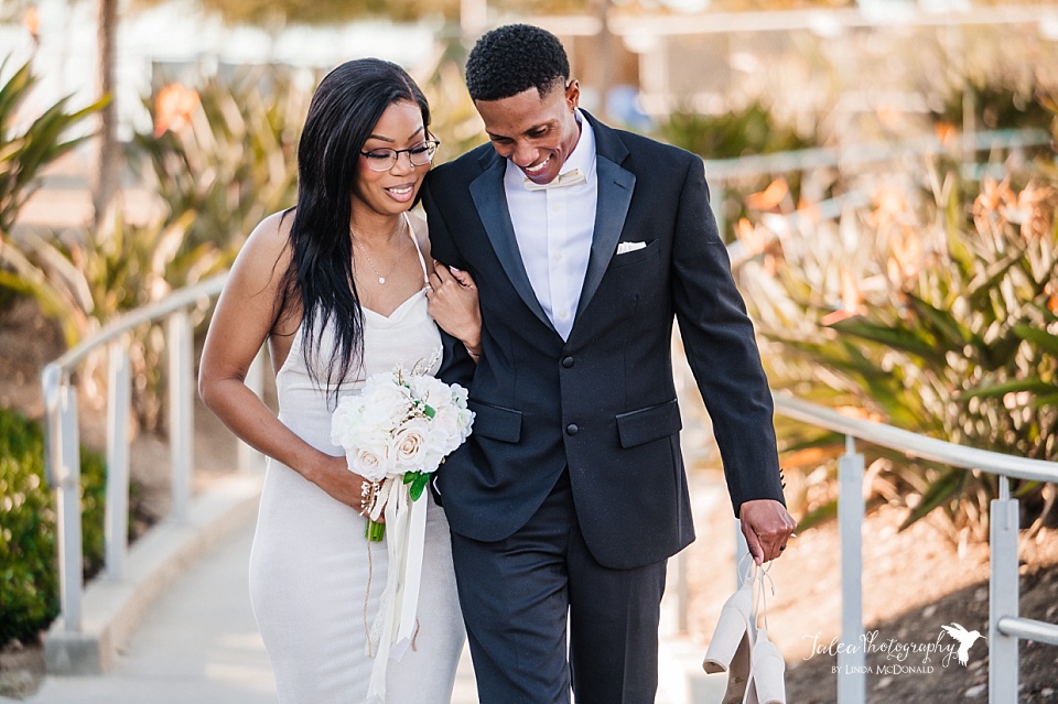 A black couple who just got married at the San Diego courthouse walk a path along some birds of paradise